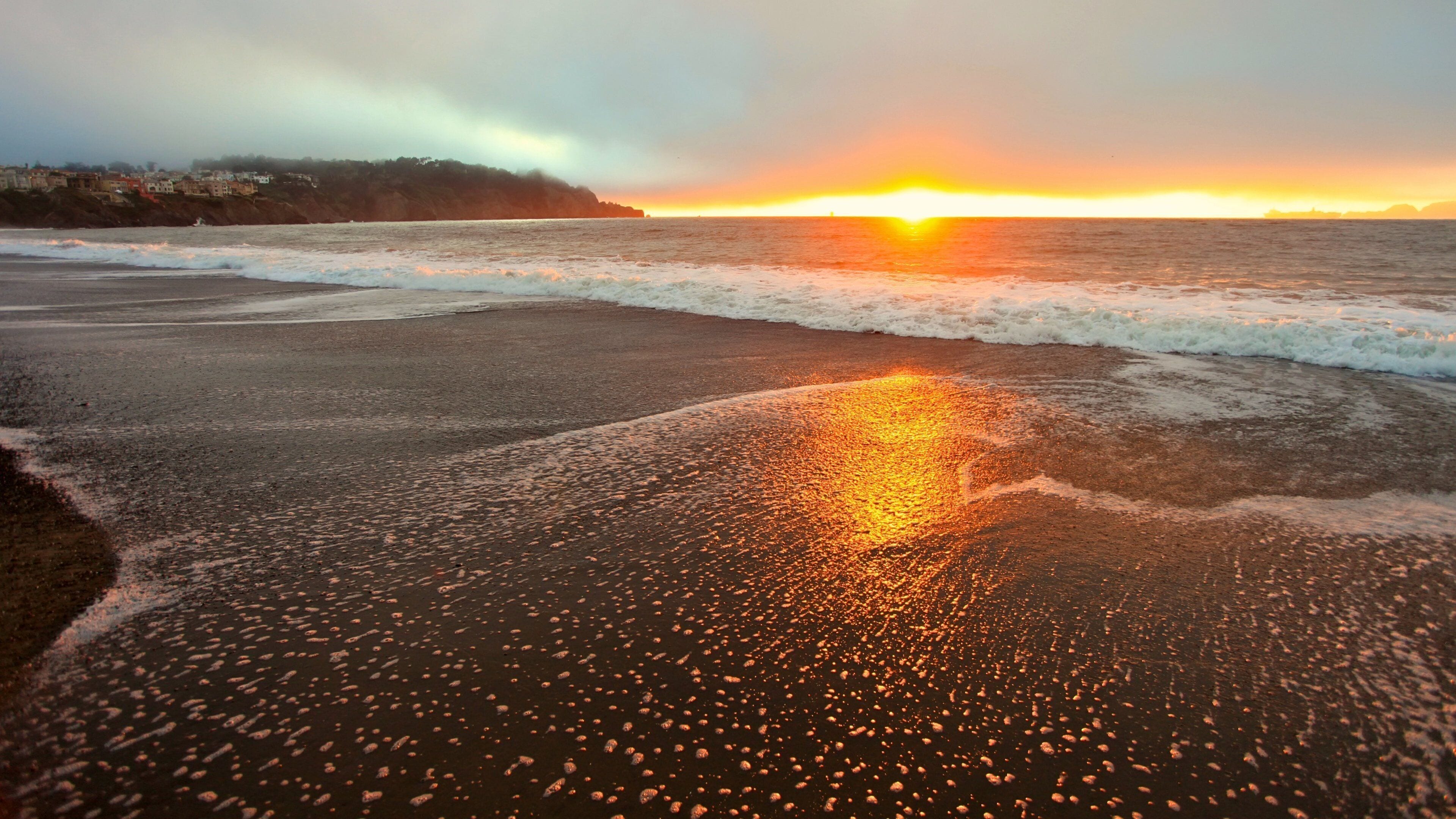 Sunset view over Baker Beach in San Francisco with waves lapping at the shore and soft clouds in the sky
