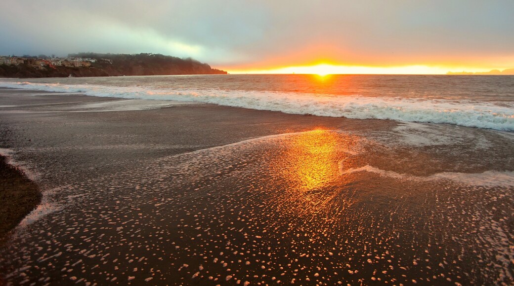 Sunset view over Baker Beach in San Francisco with waves lapping at the shore and soft clouds in the sky
