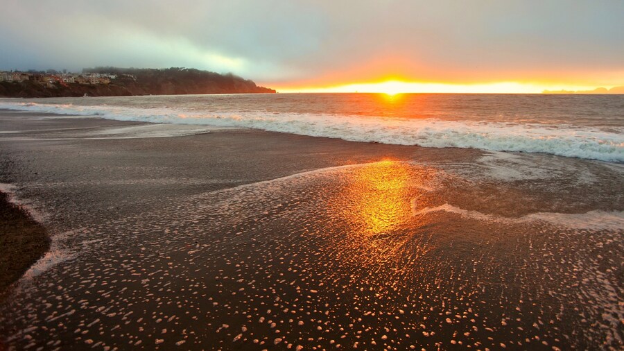 Sunset view over Baker Beach in San Francisco with waves lapping at the shore and soft clouds in the sky