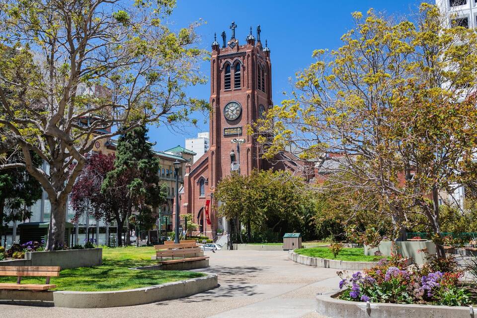 A red brick church with a clock tower, surrounded by trees and a well-maintained garden.