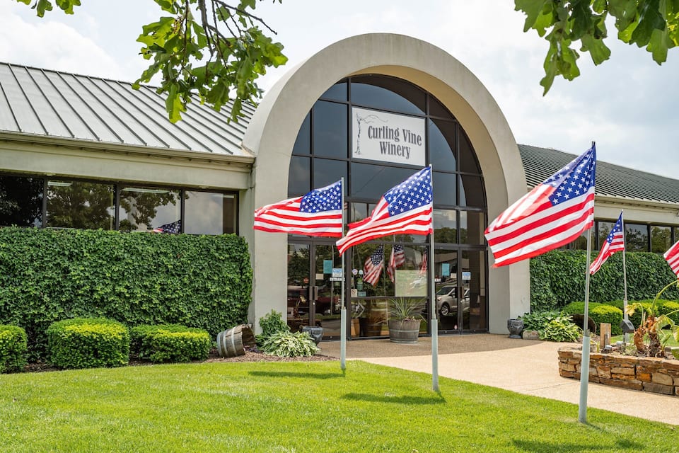 The Curling Vine Winery entrance with American flags and a well-maintained garden.