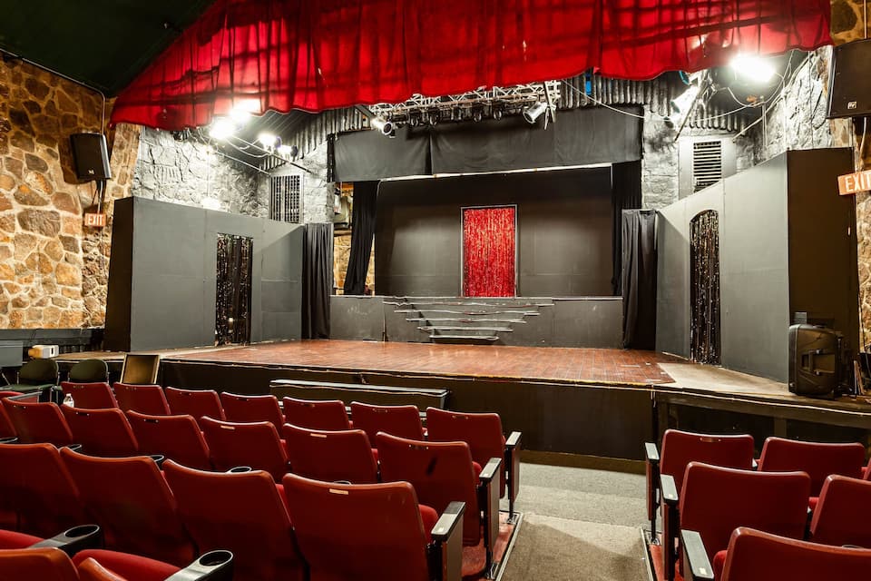 Un teatro con asientos rojos, un escenario y una pared de piedra.