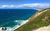 A coastal landscape with a clear blue sea, rocky cliffs, and a distant shoreline.