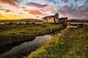 Ein verrostetes Boot am Flussufer mit Sonnenuntergang im Hintergrund.