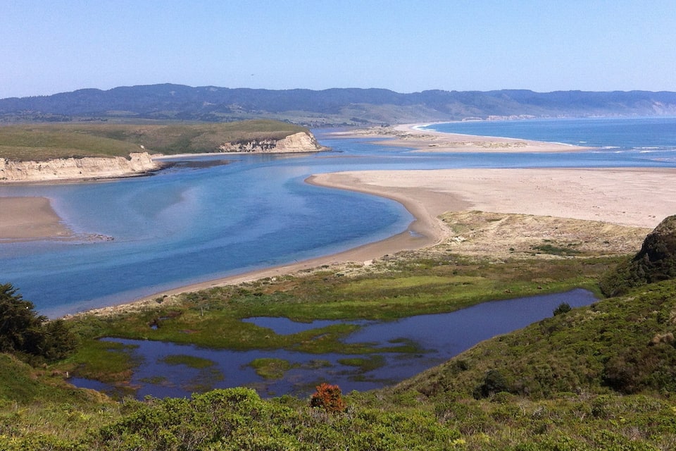 A coastal landscape with a bay, sandy beach, and green hills.
