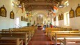 A church interior with wooden pews, a central altar, and religious statues.