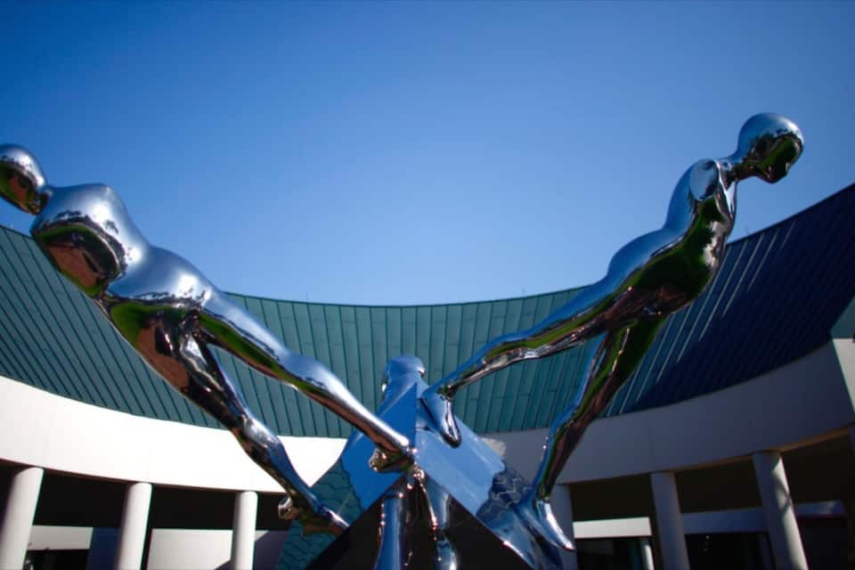 Un edificio moderno con techo curvo y una escultura de tres figuras abstractas.