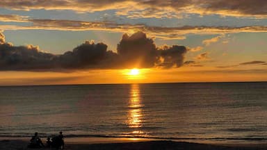 Auringonlasku tyynen meren yllä, rannalla on muutamia ihmisiä.