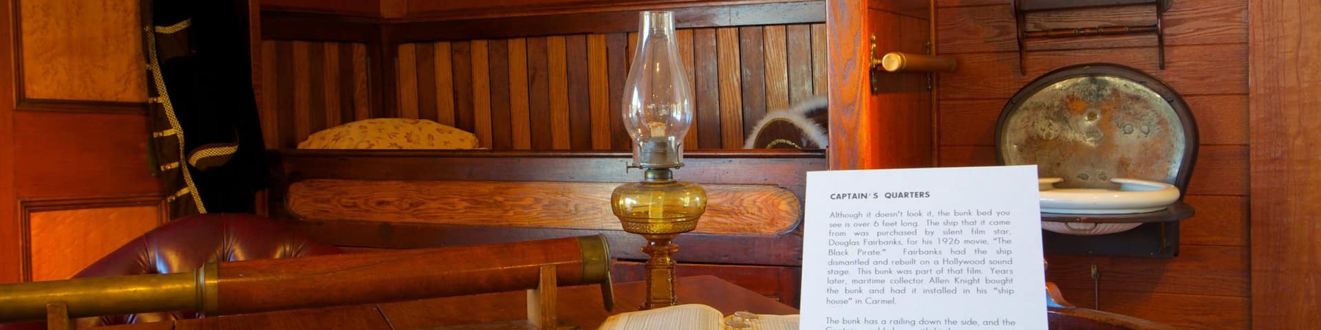 A wooden cabin interior with a bunk bed, a brass lamp, a map, and a paper describing Captain's Quarters.