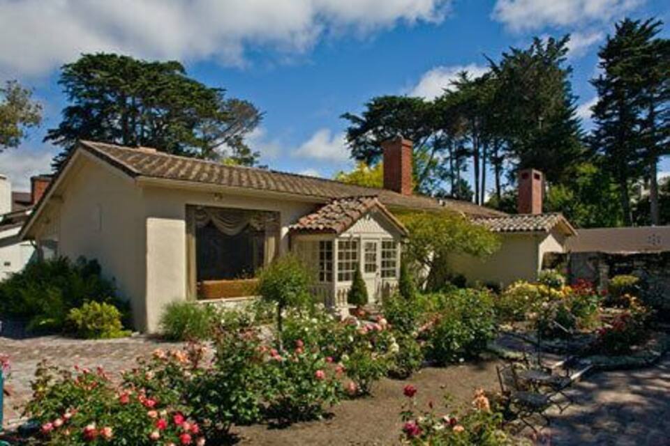 A quaint house with a tiled roof, surrounded by a garden with pink flowers and lush greenery.