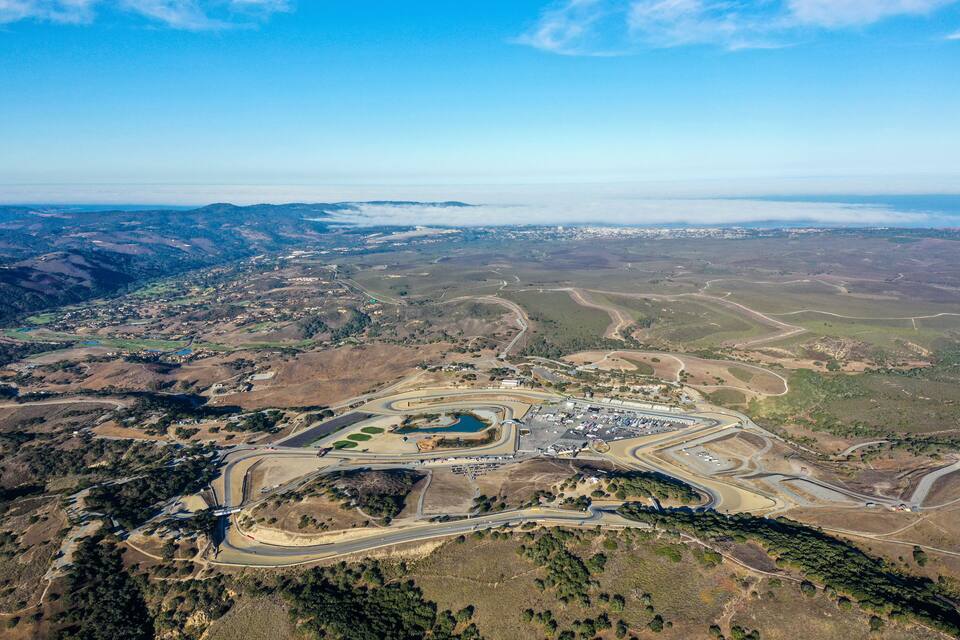 Vista aérea de uma pista de corrida cercada por terreno montanhoso e uma pequena massa de água.