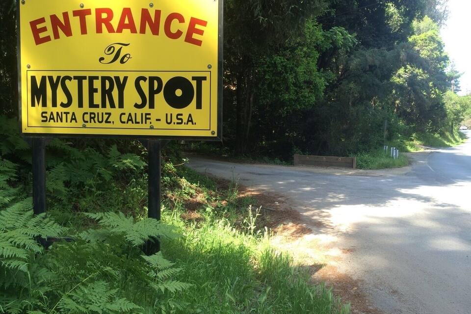 A yellow sign with red and black text reading "ENTRANCE To MYSTERY SPOT Santa Cruz, Calif. U.S.A."