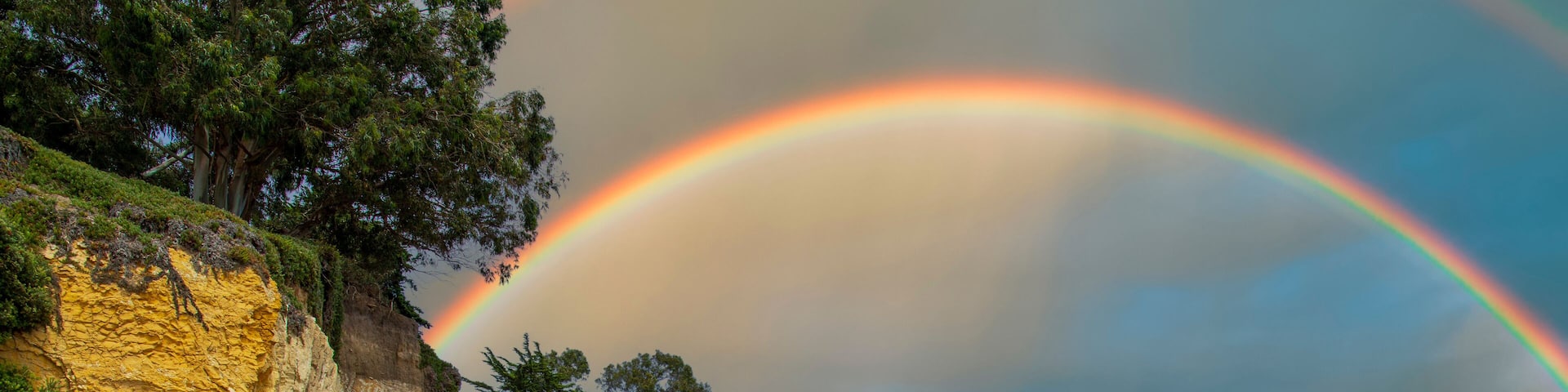 a gorgeous summer landscape at the beach with blue ocean water with waves rolling into the beach, silky brown sand and rocky cliffs covered in lush green trees and plants and blue sky and clouds