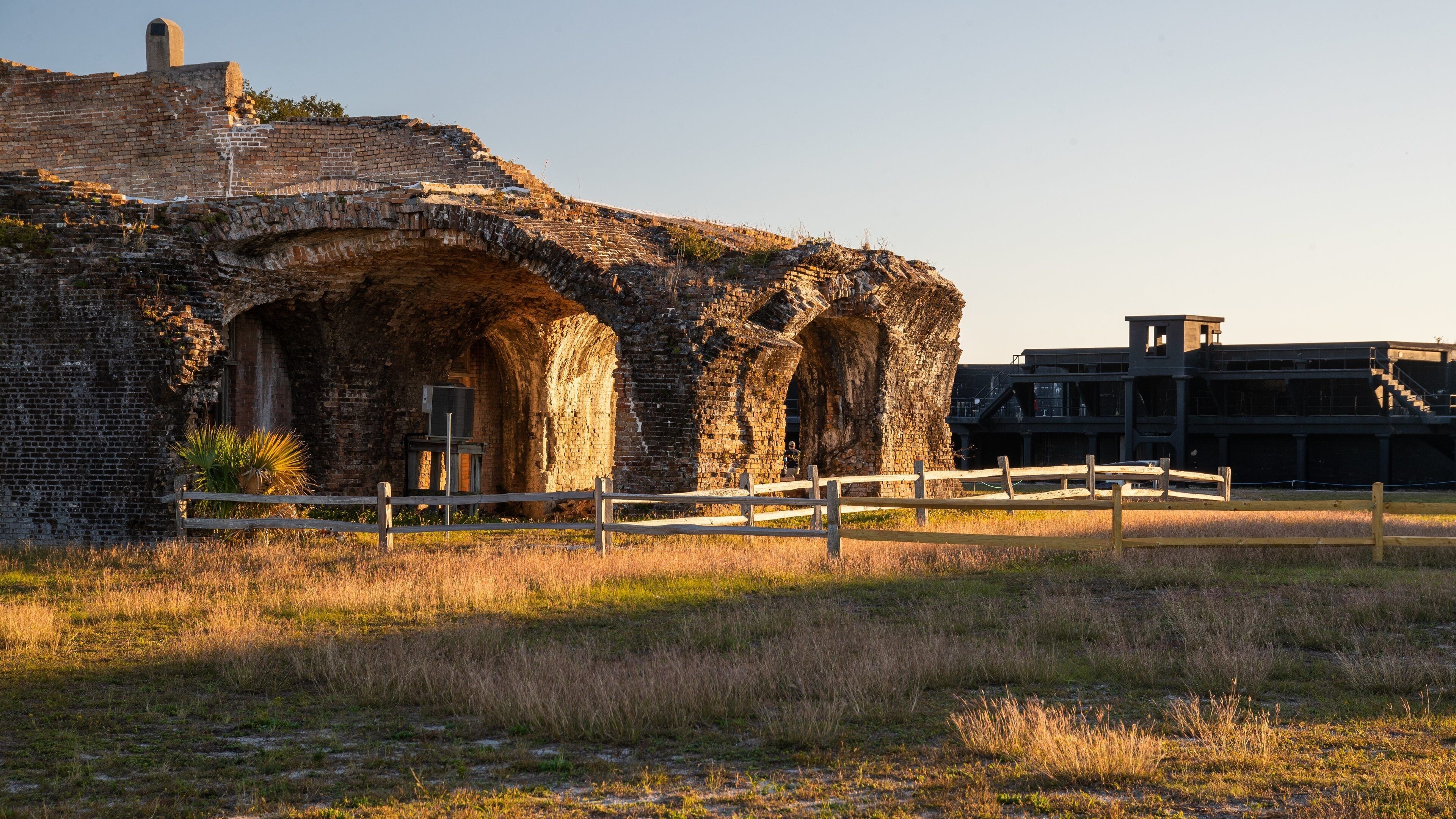 An ancient brick structure with arched doorways and a modern building in the background.