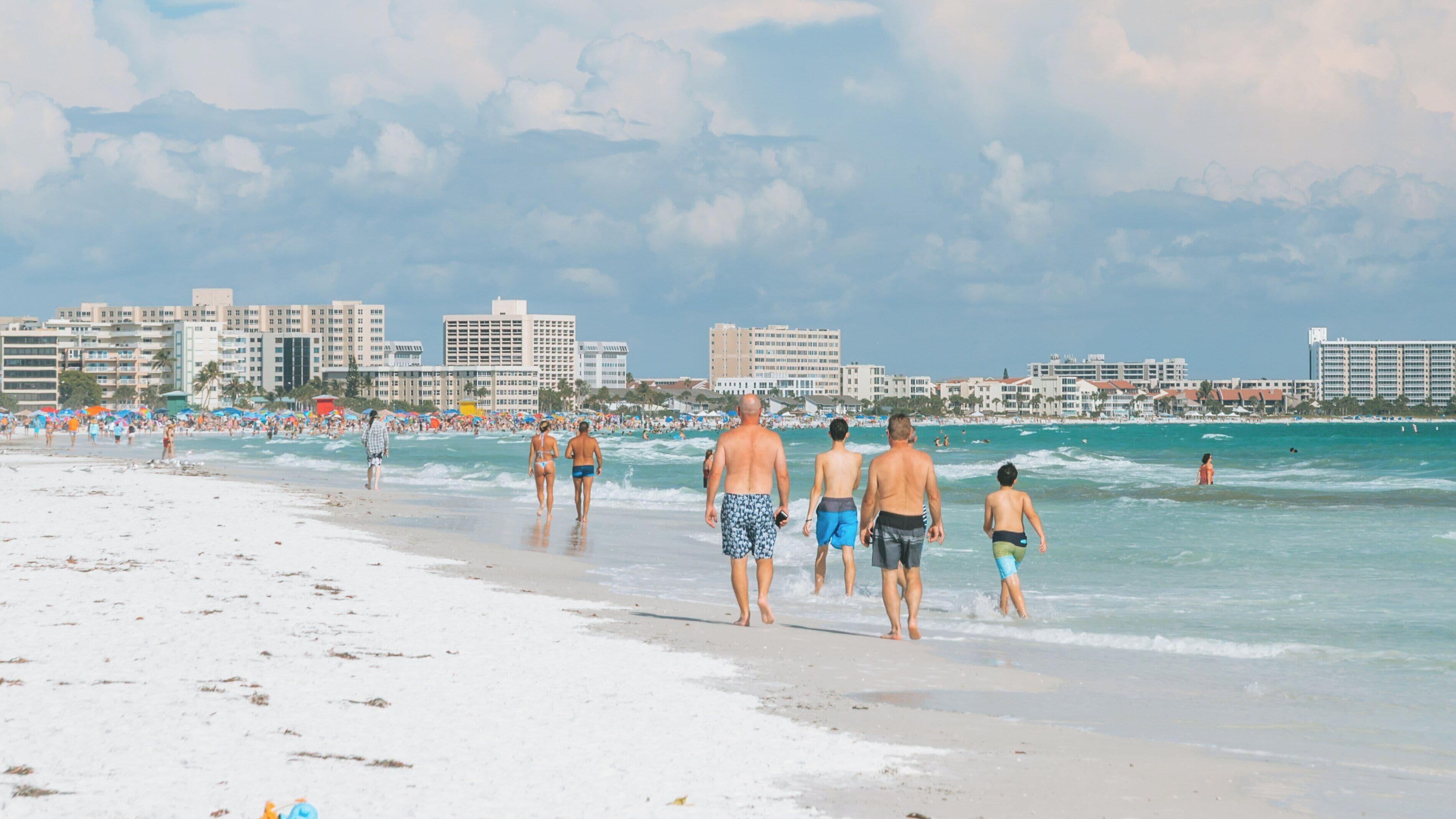 Visitors enjoy a sunny day walking along the white sandy shores of Siesta Key Beach in Florida near clear turquoise waters