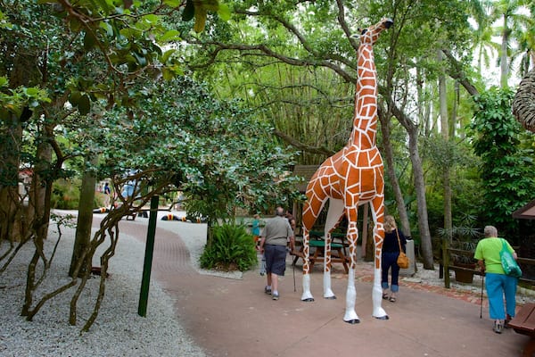 A giraffe statue in a park with trees and people around.