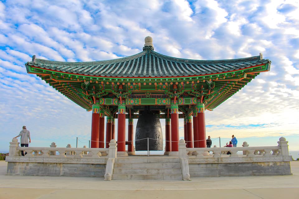 A traditional Korean pavilion with ornate roof and columns, set against a partly cloudy sky.