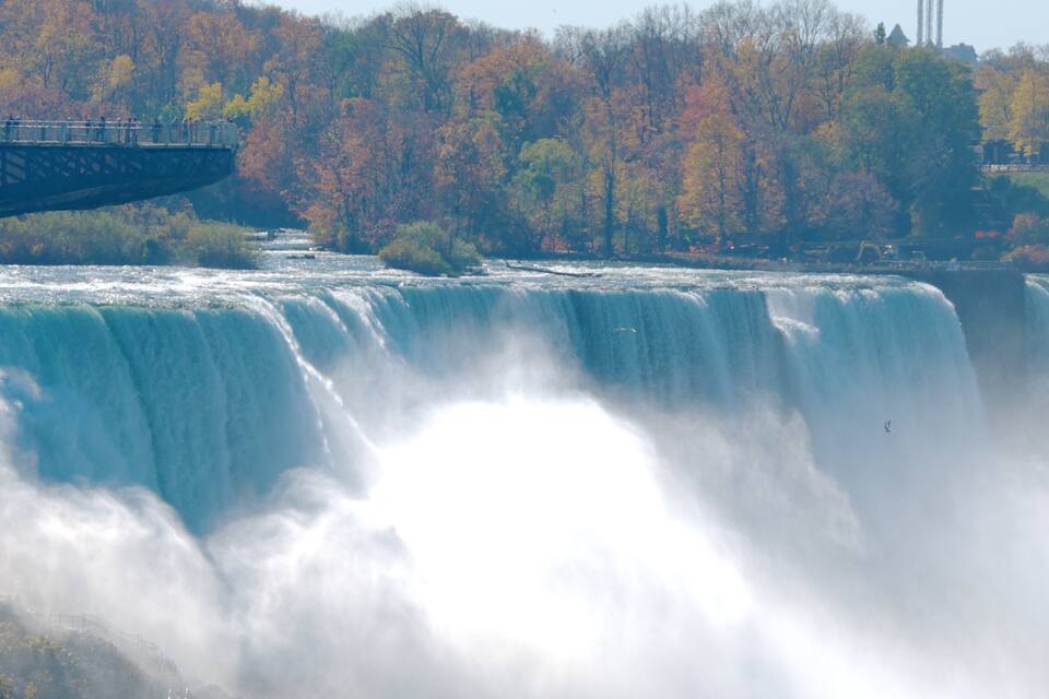 A large waterfall with a viewing platform and autumn-colored trees in the background.
