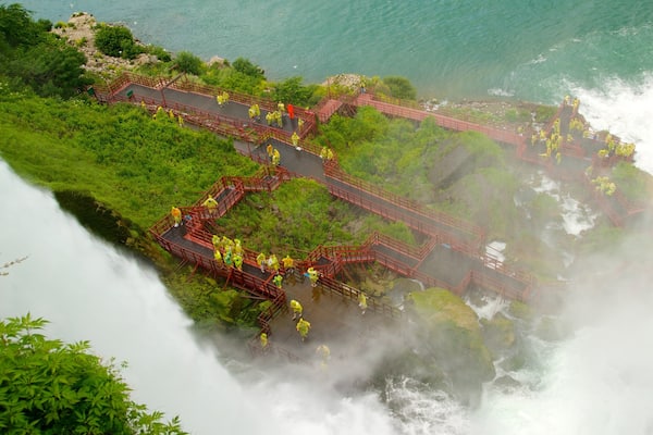 Uma cascata com uma ponte vermelha e pessoas de impermeáveis amarelos.