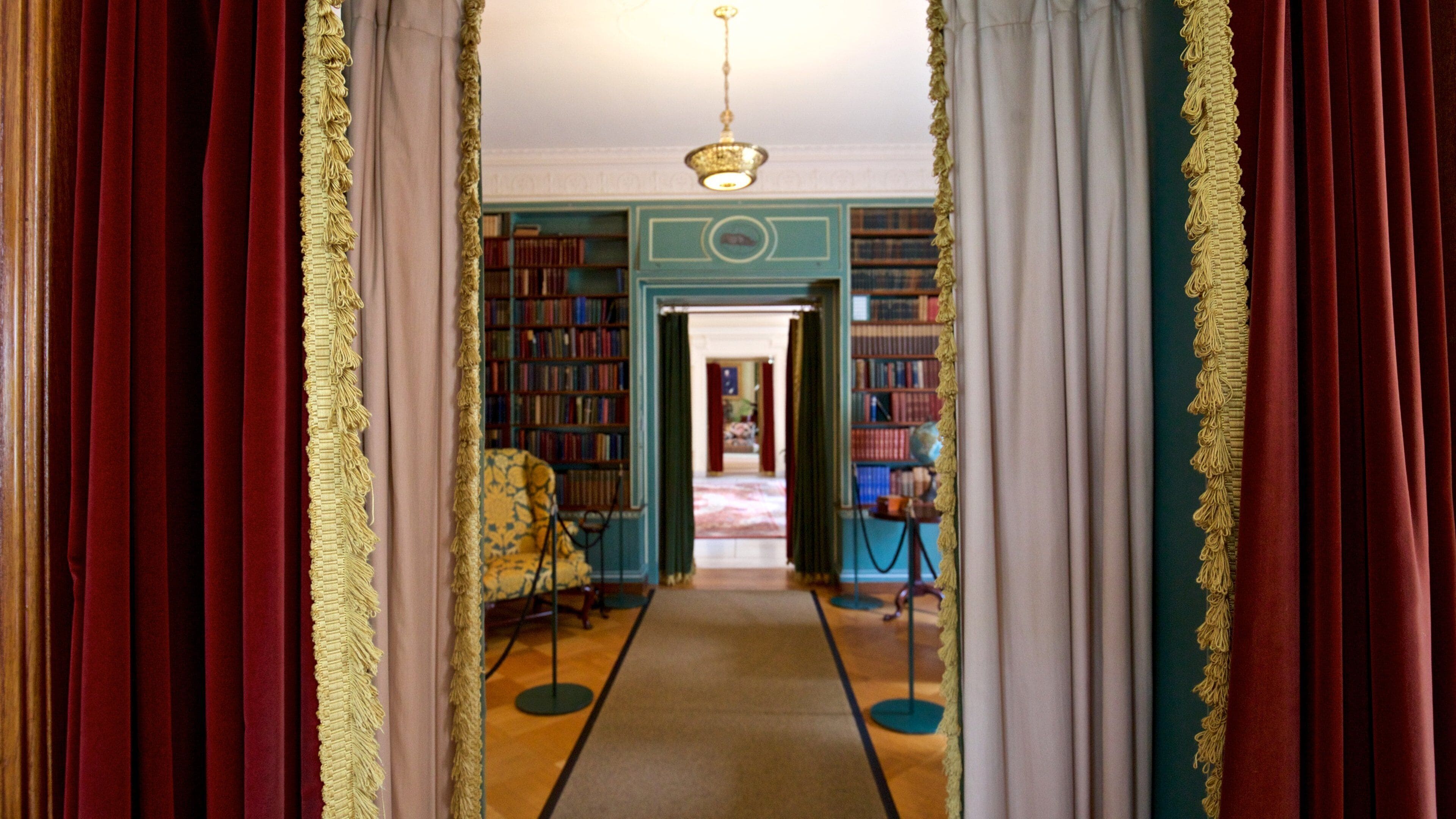 A grand hallway with red and white drapes, a chandelier, and bookshelves filled with books.