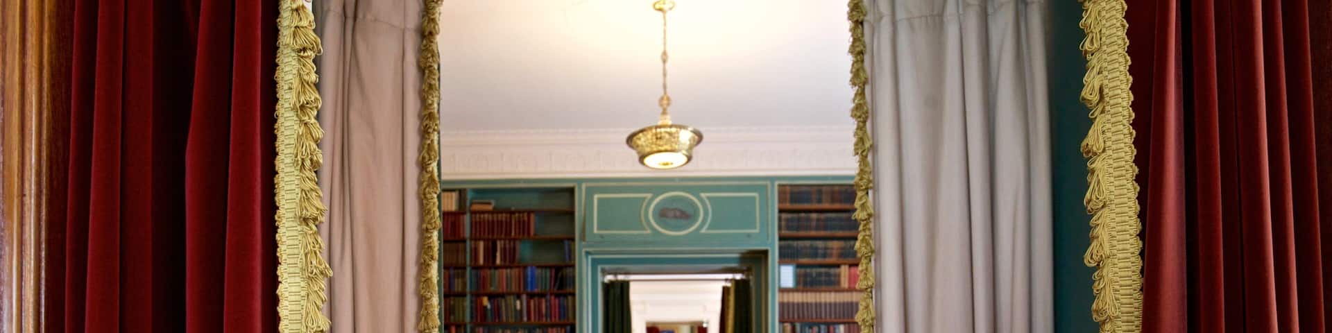 A grand hallway with red and white drapes, a chandelier, and bookshelves filled with books.