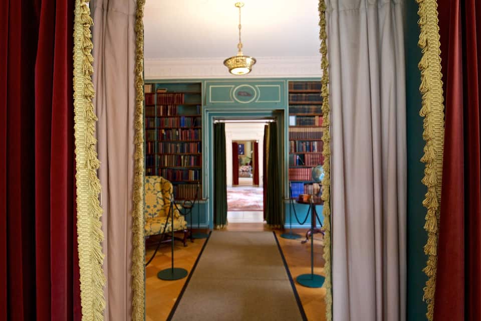 A grand hallway with red and white drapes, a chandelier, and bookshelves filled with books.