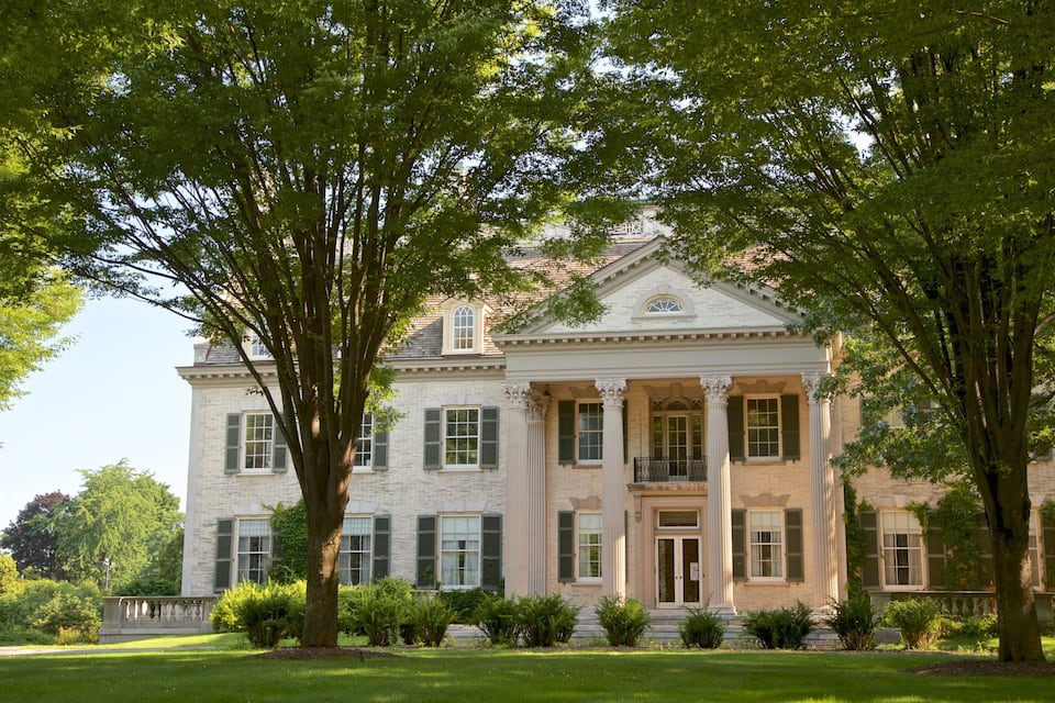 Un grand bâtiment imposant, doté d’une façade classique, entouré d’une végétation luxuriante et d’arbres.