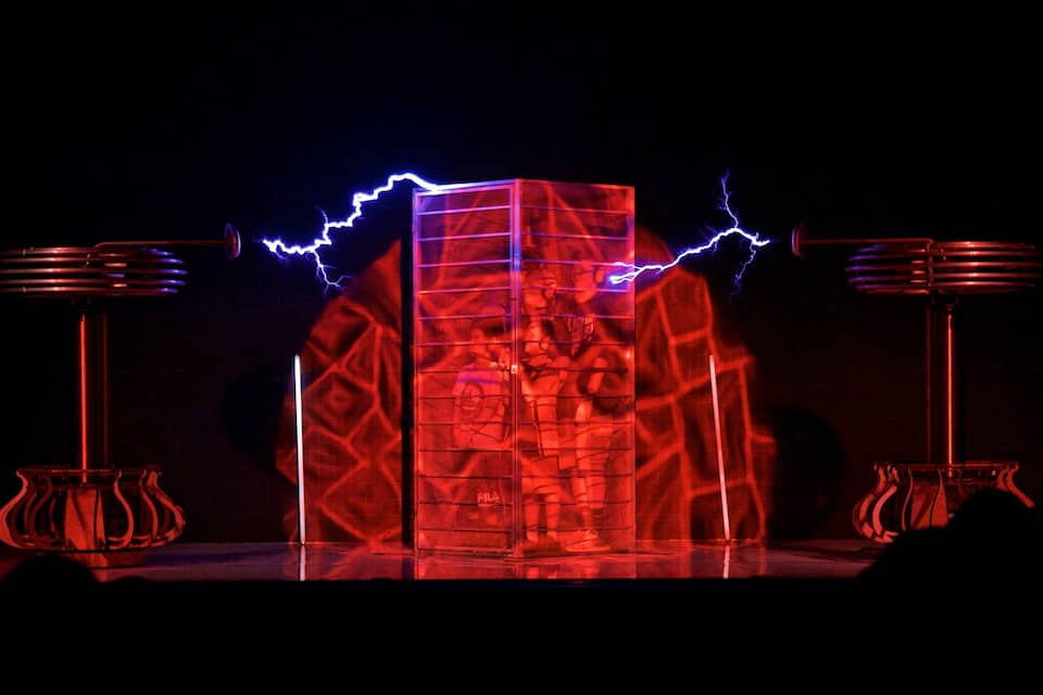 A red-lit structure with a grid pattern, flanked by two tall, cylindrical objects with horizontal lines.