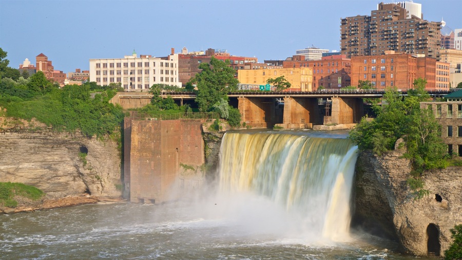 A waterfall cascading over a rocky cliff with a bridge and buildings in the background.