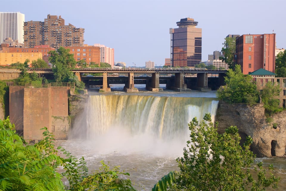 A waterfall, a bridge, and city buildings in the background.