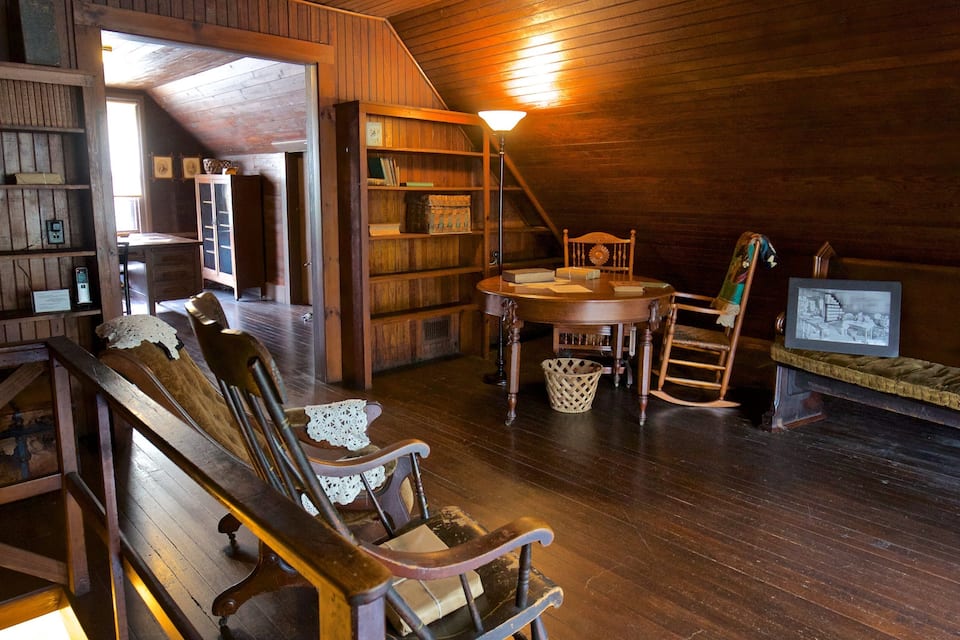 A wooden interior with a loft bed, a table, chairs, and a bookshelf.