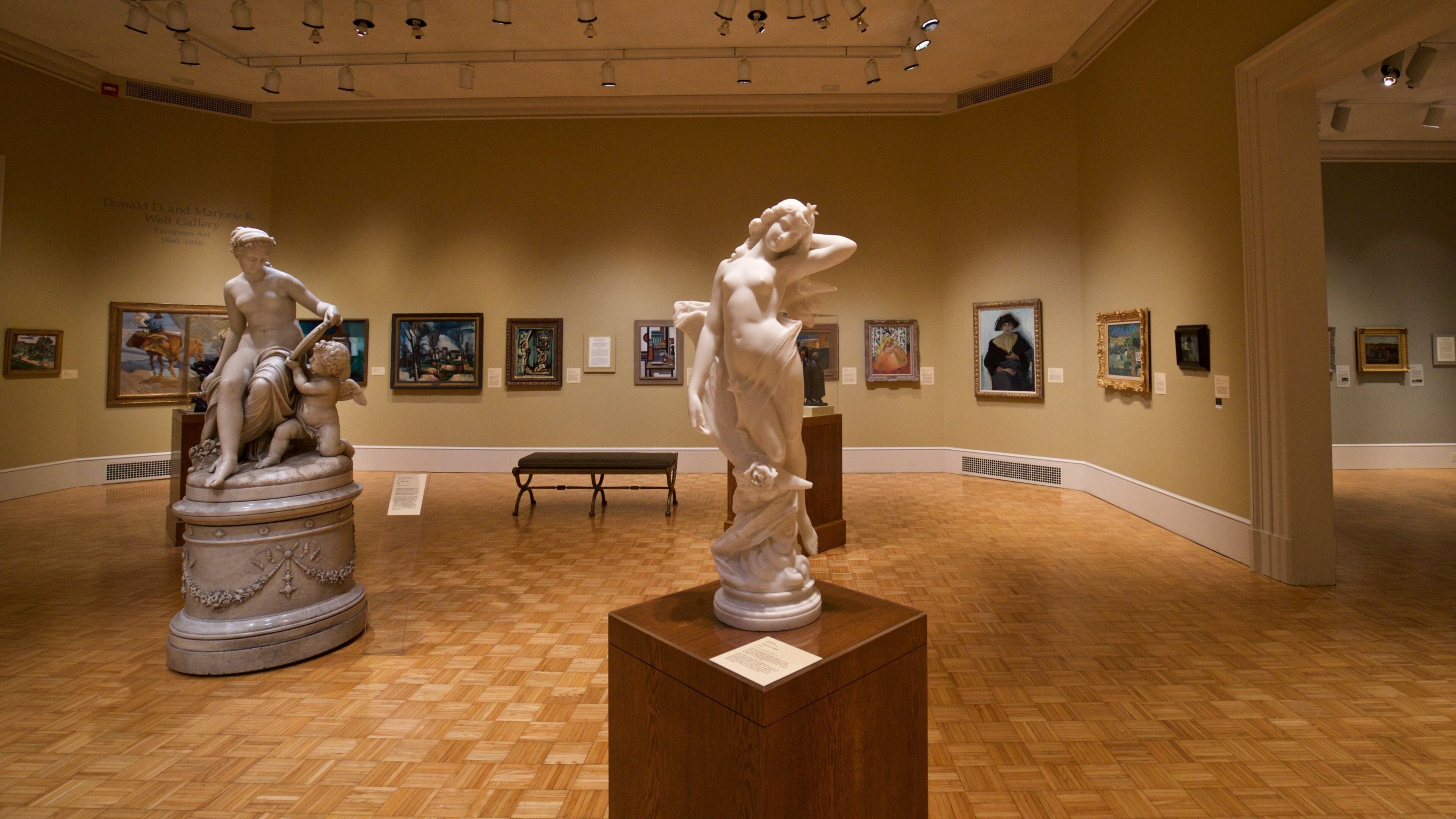 A museum interior with classical sculptures and framed paintings on the walls.
