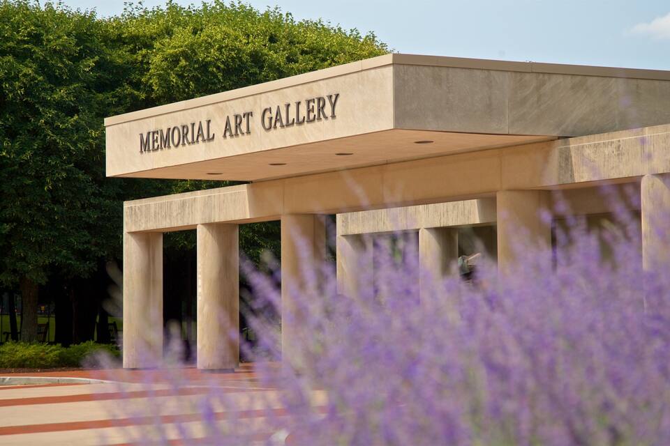 A building labeled "Memorial Art Gallery" with a modern architectural design, surrounded by trees and purple flowers.