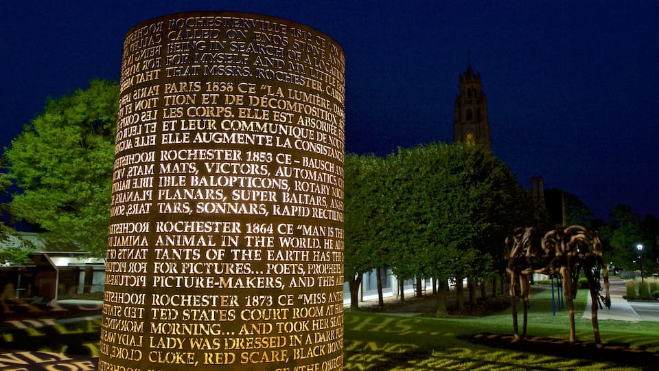 A cylindrical illuminated structure with historical text, set against a night sky with a church tower in the background.