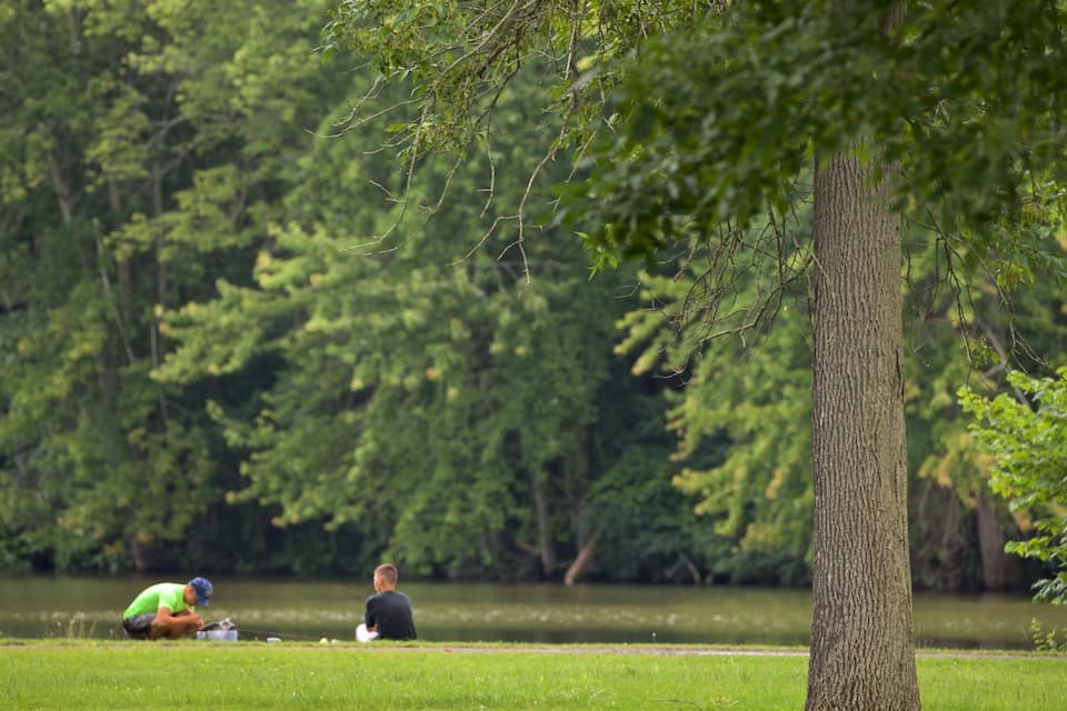 A lake with two people fishing, surrounded by dense green trees.
