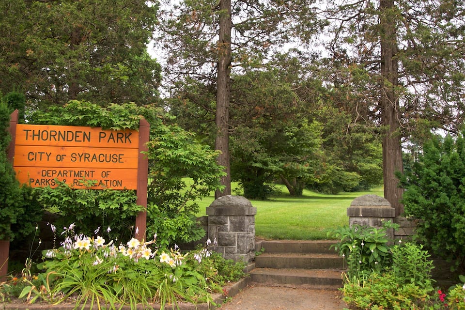 A sign for Thornden Park in Syracuse, surrounded by lush greenery and a stone pathway.