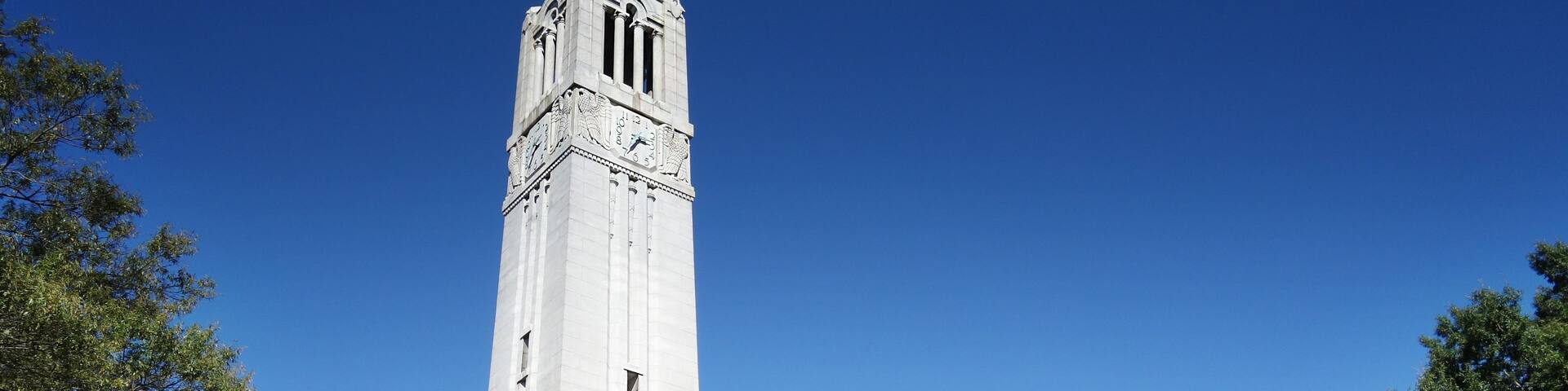 A tall white tower with a clock and a flag.