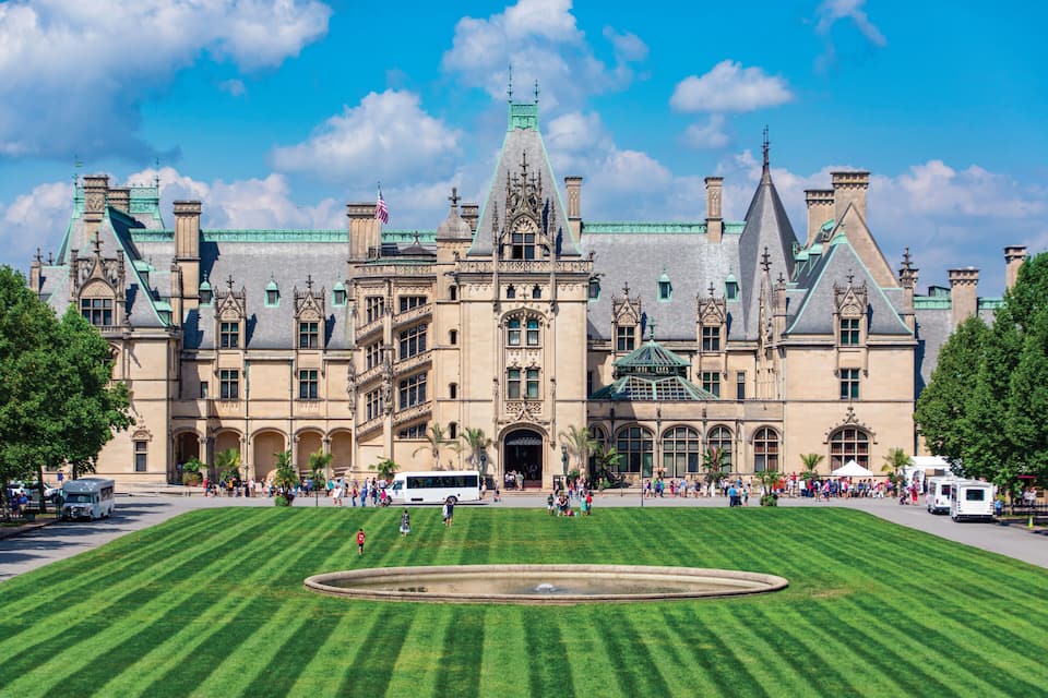A historic building with a large lawn and a fountain in front.