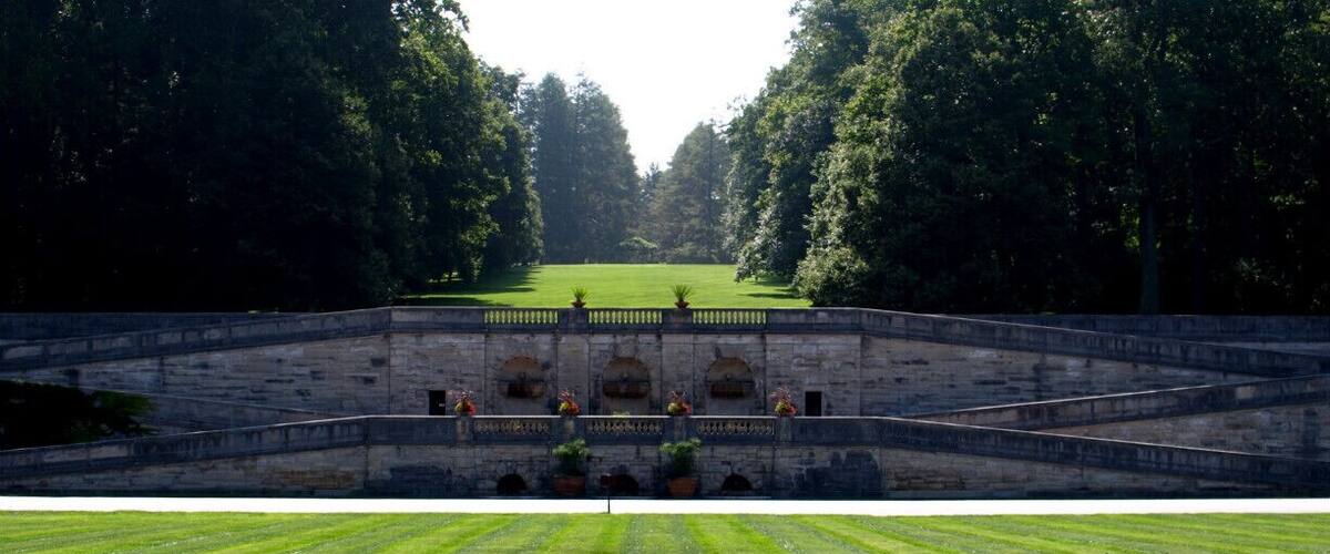 A formal garden with a central lawn, stone walls, and trees.