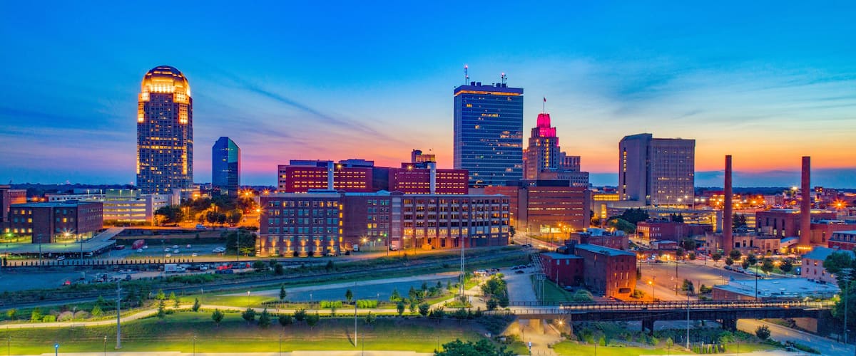 A city skyline at dusk with illuminated buildings and a bridge.