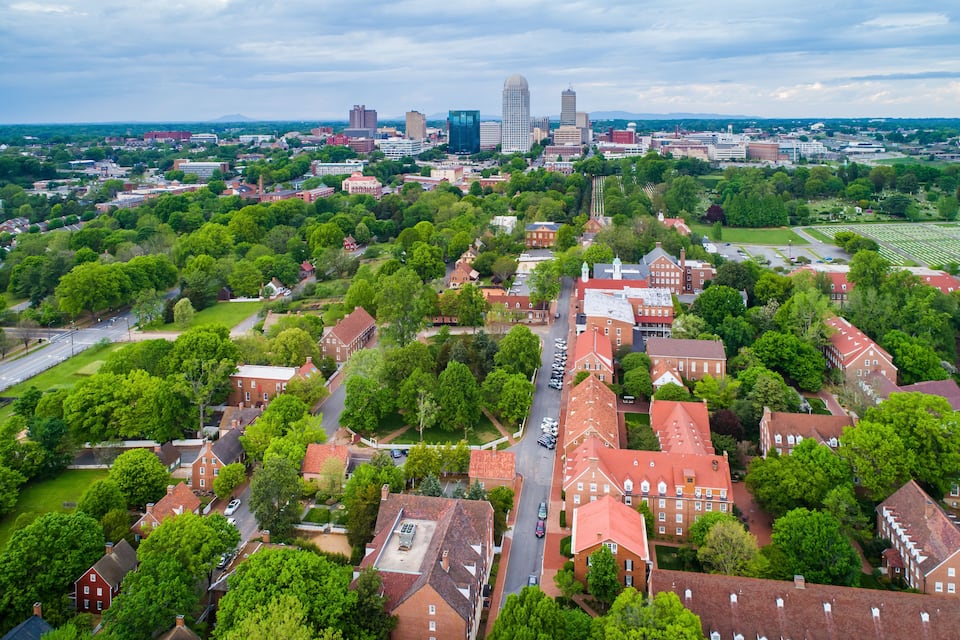 An aerial view of a city with red-roofed buildings, green parks, and a distant city skyline.