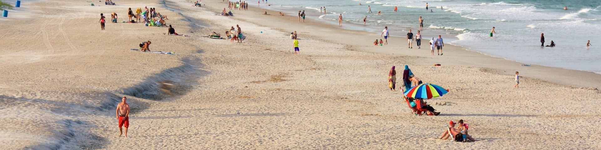 A crowded beach with people sunbathing, walking, and playing in the water.