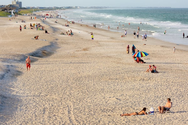 Une plage bondée où les gens se prélassent au soleil, se promènent et jouent dans l’eau.