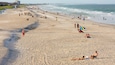 Ein überfüllter Strand mit Menschen, die sich sonnen, spazieren gehen und im Wasser spielen.