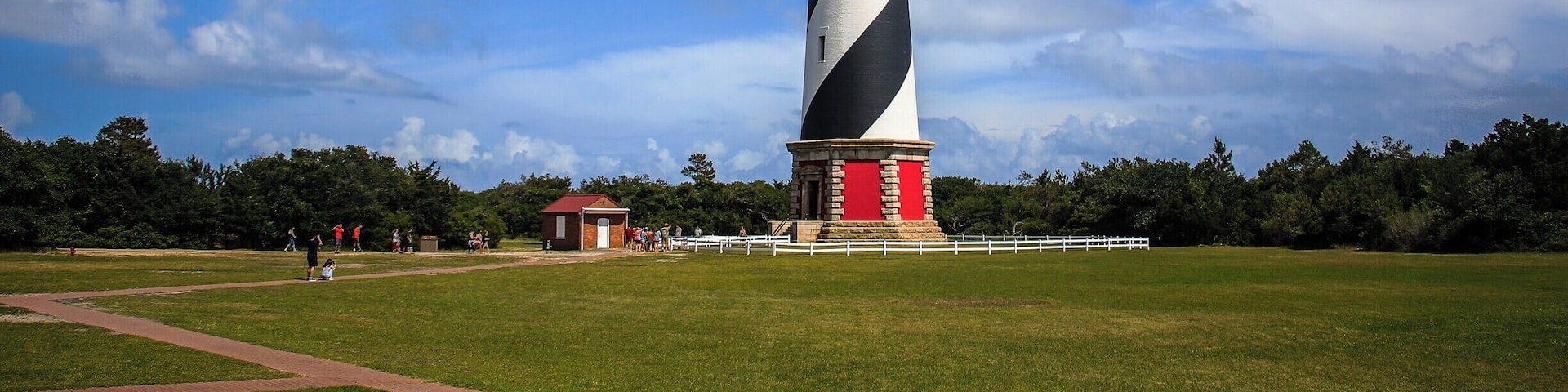 A tall lighthouse with black and white stripes, surrounded by a grassy field and trees.