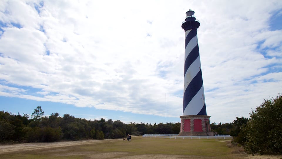 A tall lighthouse with a black and white striped pattern, surrounded by a white fence and a grassy field.
