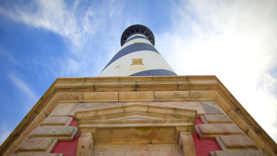 A lighthouse with a white and blue striped tower and a stone base.