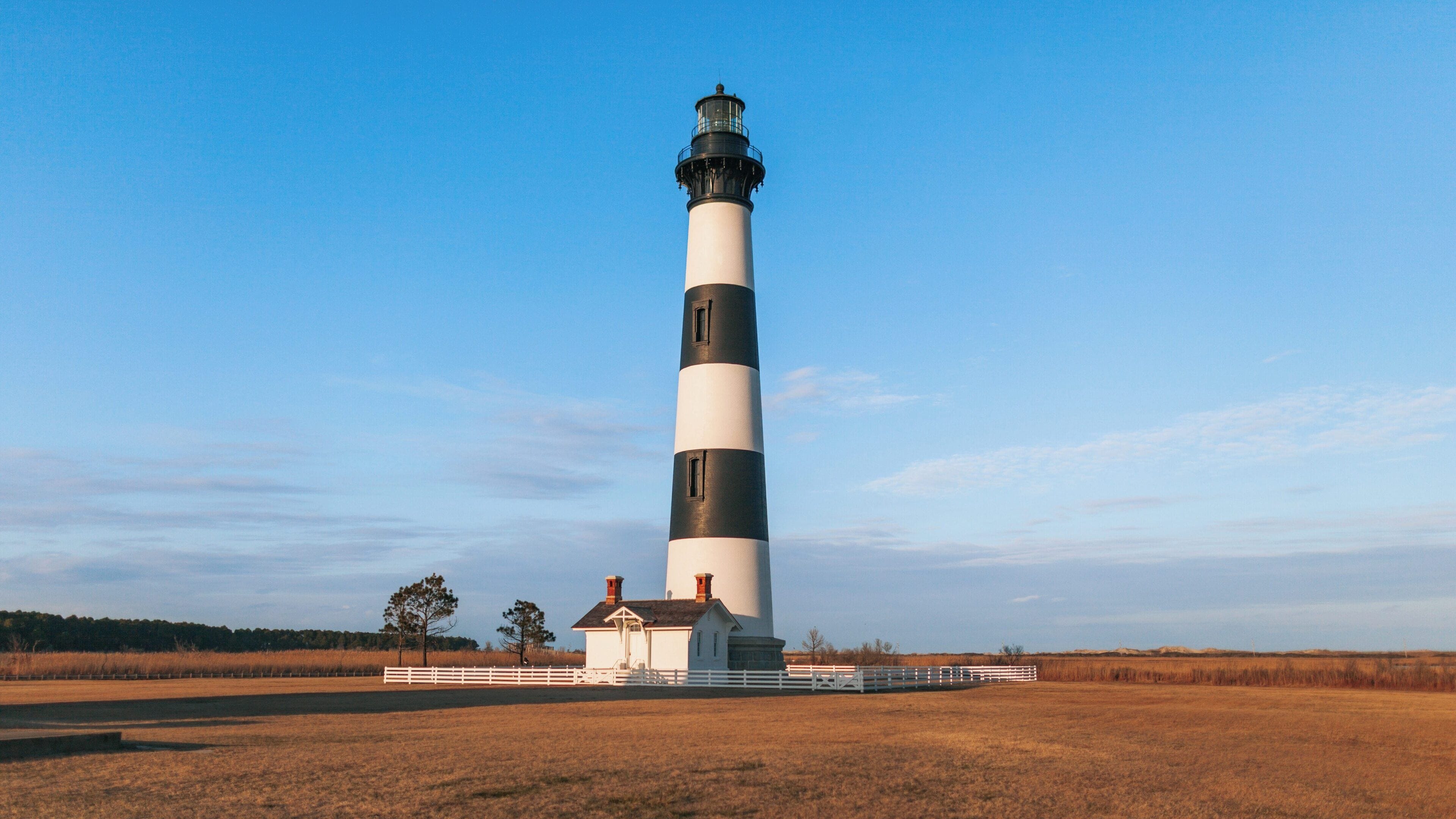 Bodie Island Lighthouse standing tall against a clear blue sky in South Nags Head, North Carolina, showcasing its historic design and surrounding landscape