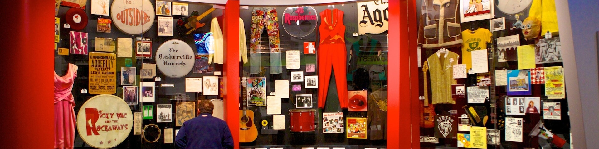 Exposição de museu intitulada 'Cleveland Rocks' com objetos de coleção, cartazes e um manequim calçado com calças vermelhas.