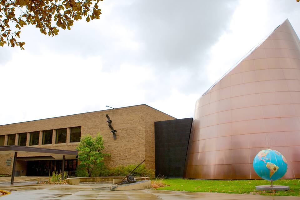 A modern building with a curved metallic facade and a globe sculpture in front.